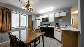 A modern kitchen with white cabinets, a microwave, stove, and dishwasher. There is a dining table with chairs and a chandelier.