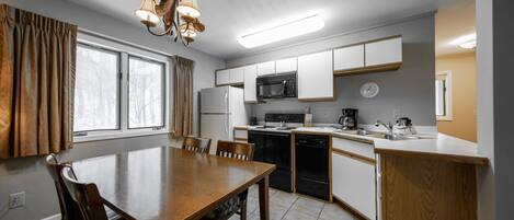 Une cuisine moderne avec des meubles blancs, un four à micro-ondes, une cuisinière et un lave-vaisselle. On y trouve une table à manger avec des chaises et un lustre.