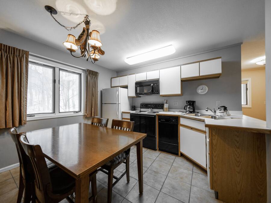A modern kitchen with white cabinets, a microwave, stove, and dishwasher. There is a dining table with chairs and a chandelier.