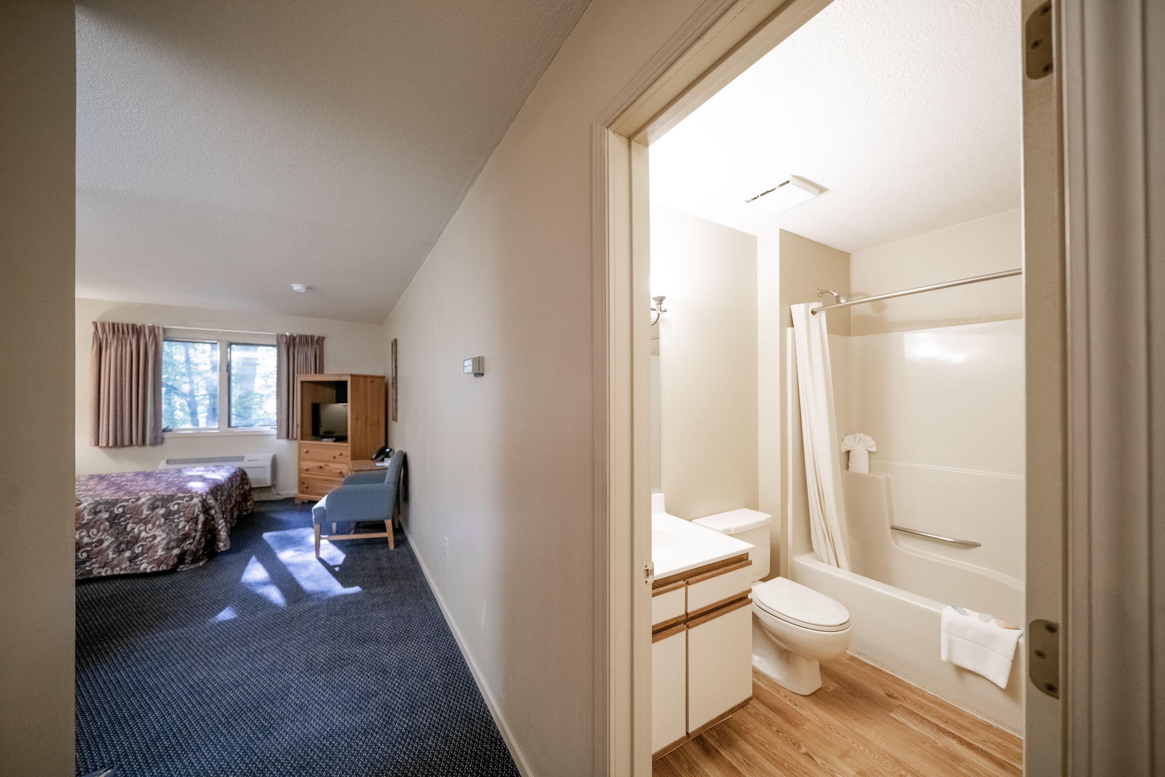 Ein Schlafzimmer mit Bett, Schreibtisch und Stuhl. Es gibt ein Badezimmer mit Toilette, Waschbecken und Dusche.
