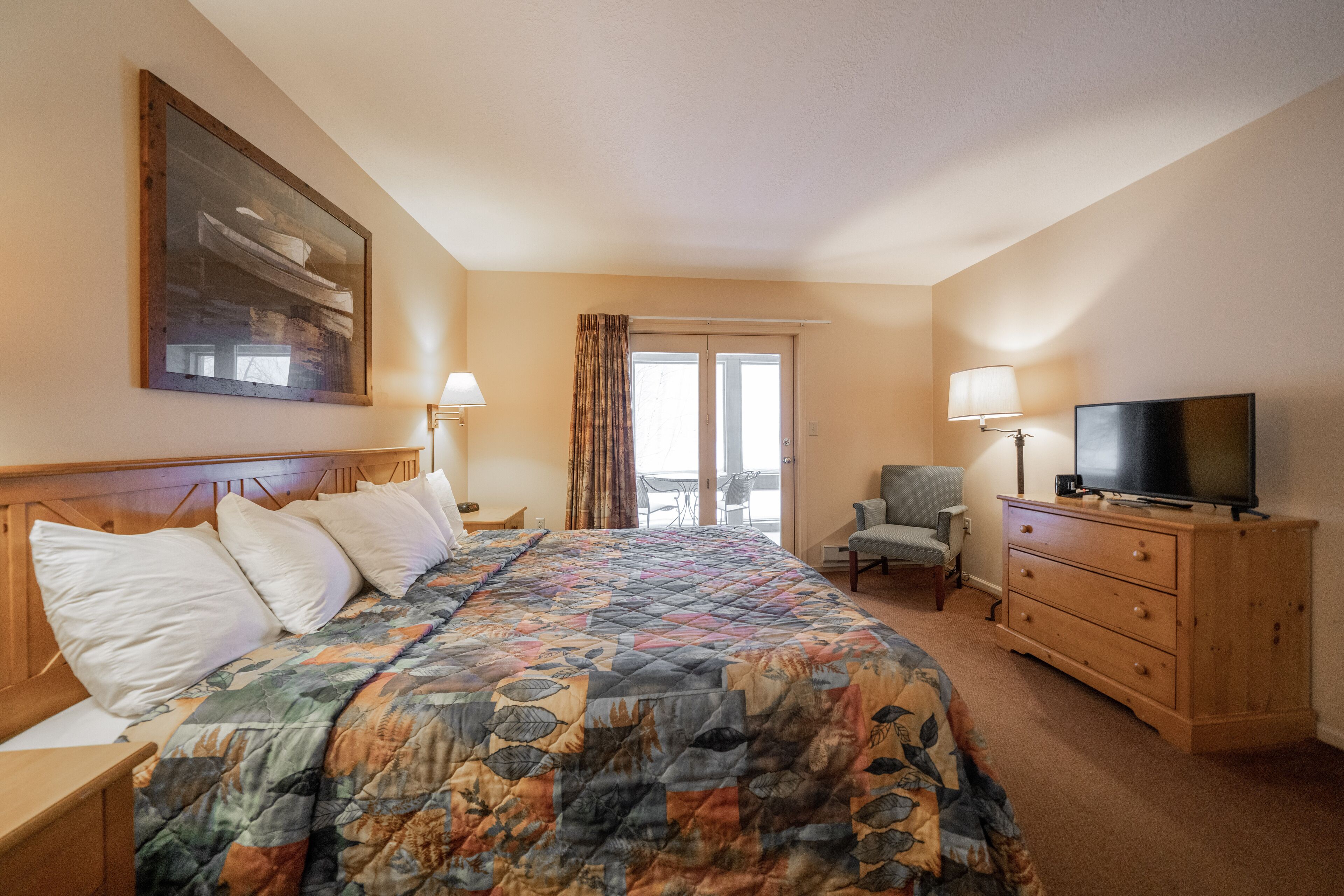 Une chambre d’hôtel avec un grand lit, un téléviseur posé sur une commode, une chaise et un balcon avec des rideaux.