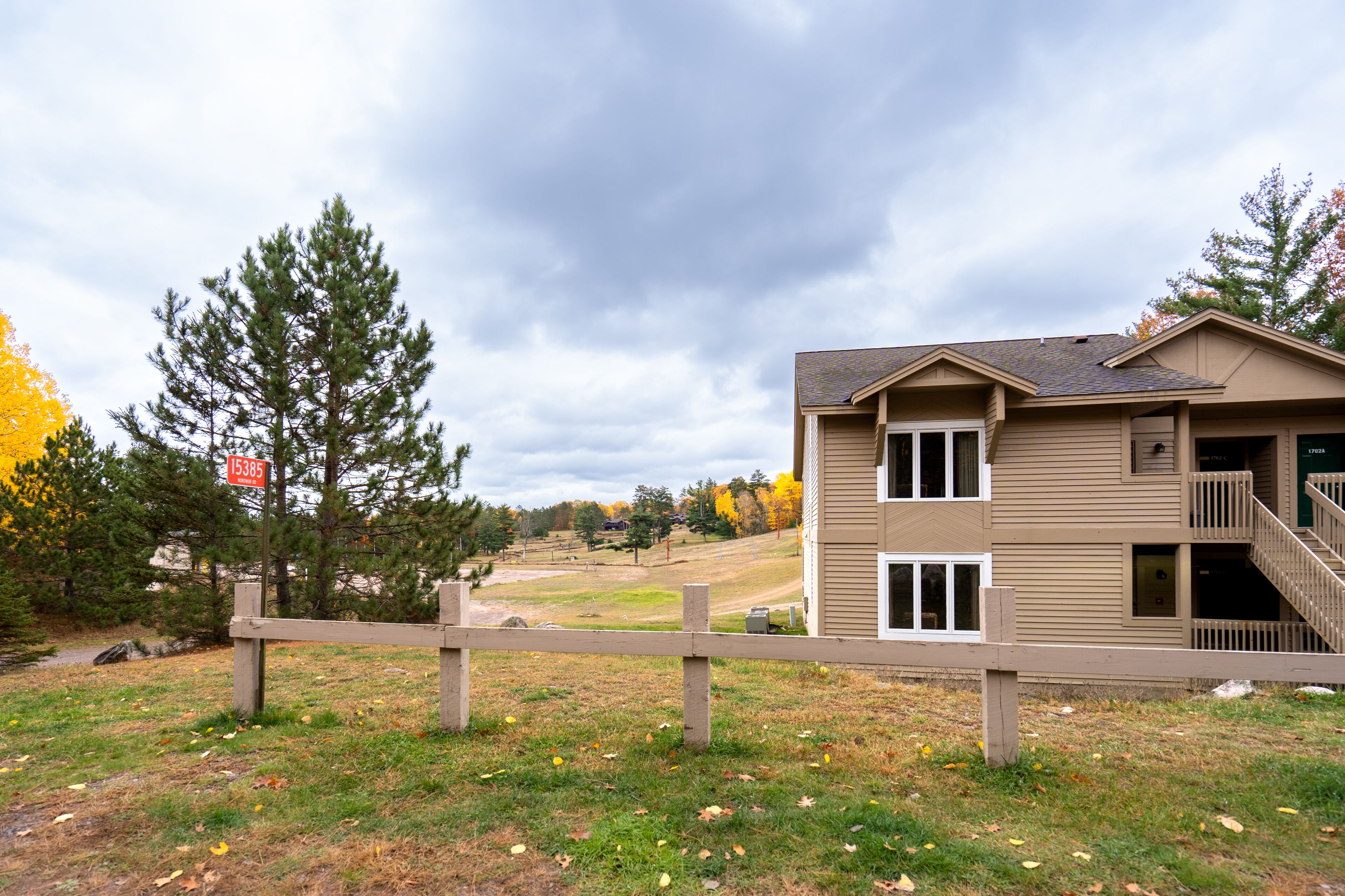 A two-story building with a balcony, a fenced area, and a view of a hilly landscape.