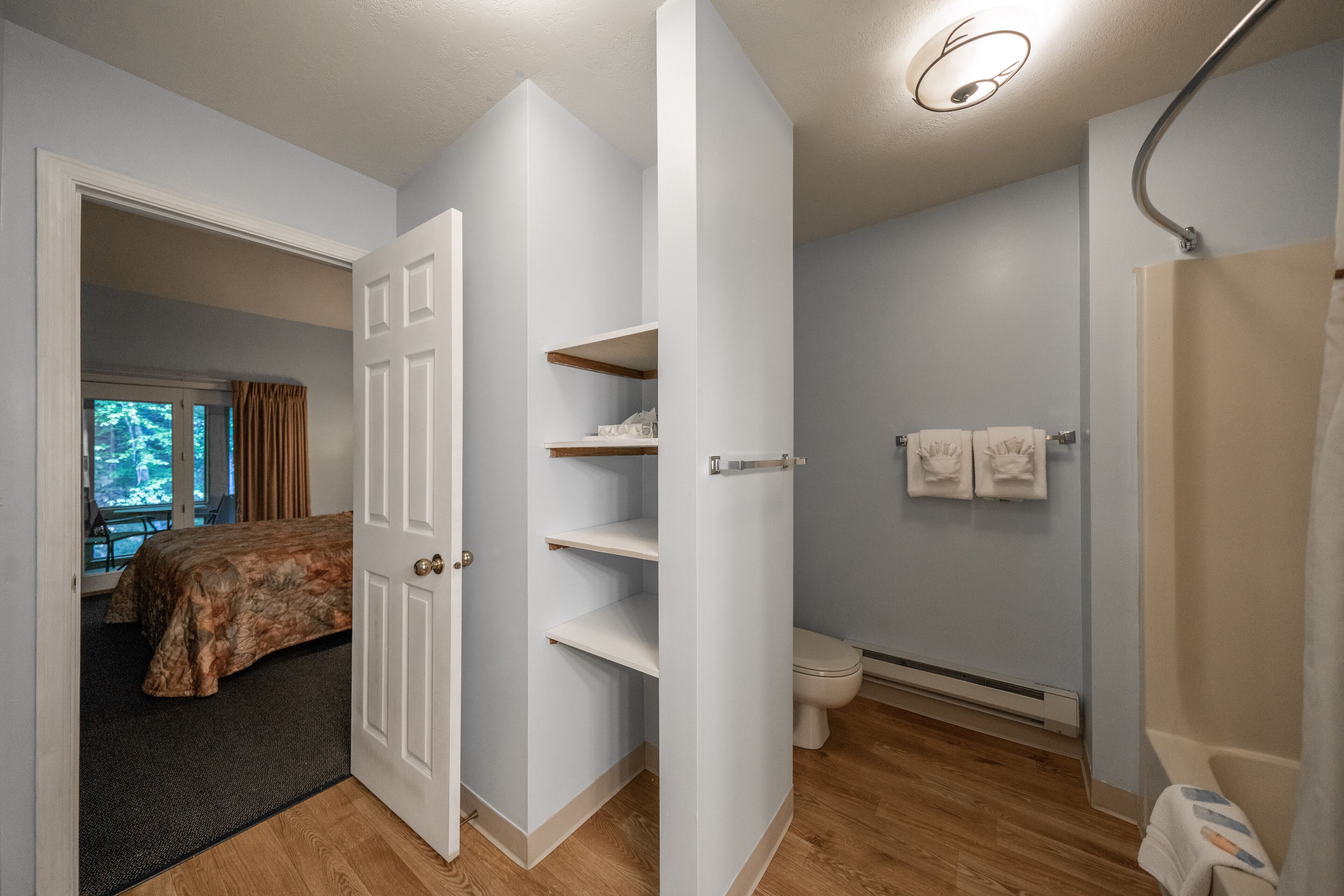 Una habitación con una cama, un inodoro y una ducha. Hay una puerta que conduce a otra habitación.