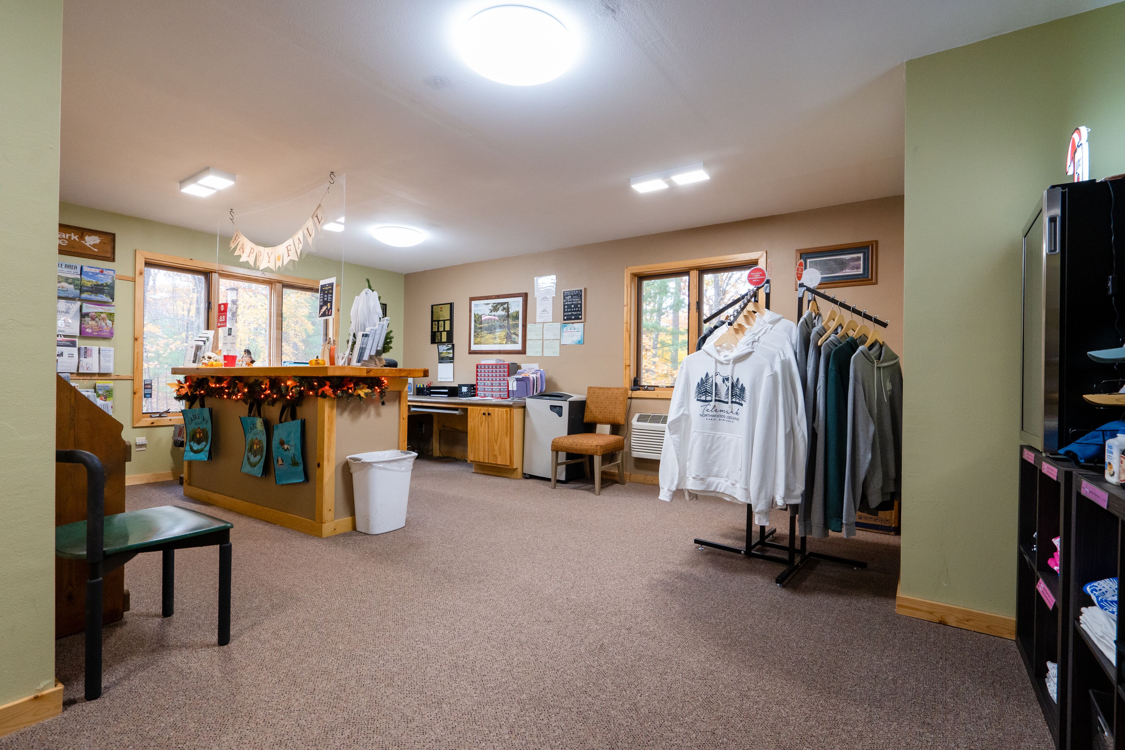 A room with a reception desk, a coat rack with hanging clothes, a chair, and a small table with a basket.