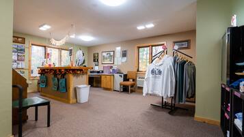A room with a reception desk, a coat rack with hanging clothes, a chair, and a small table with a basket.