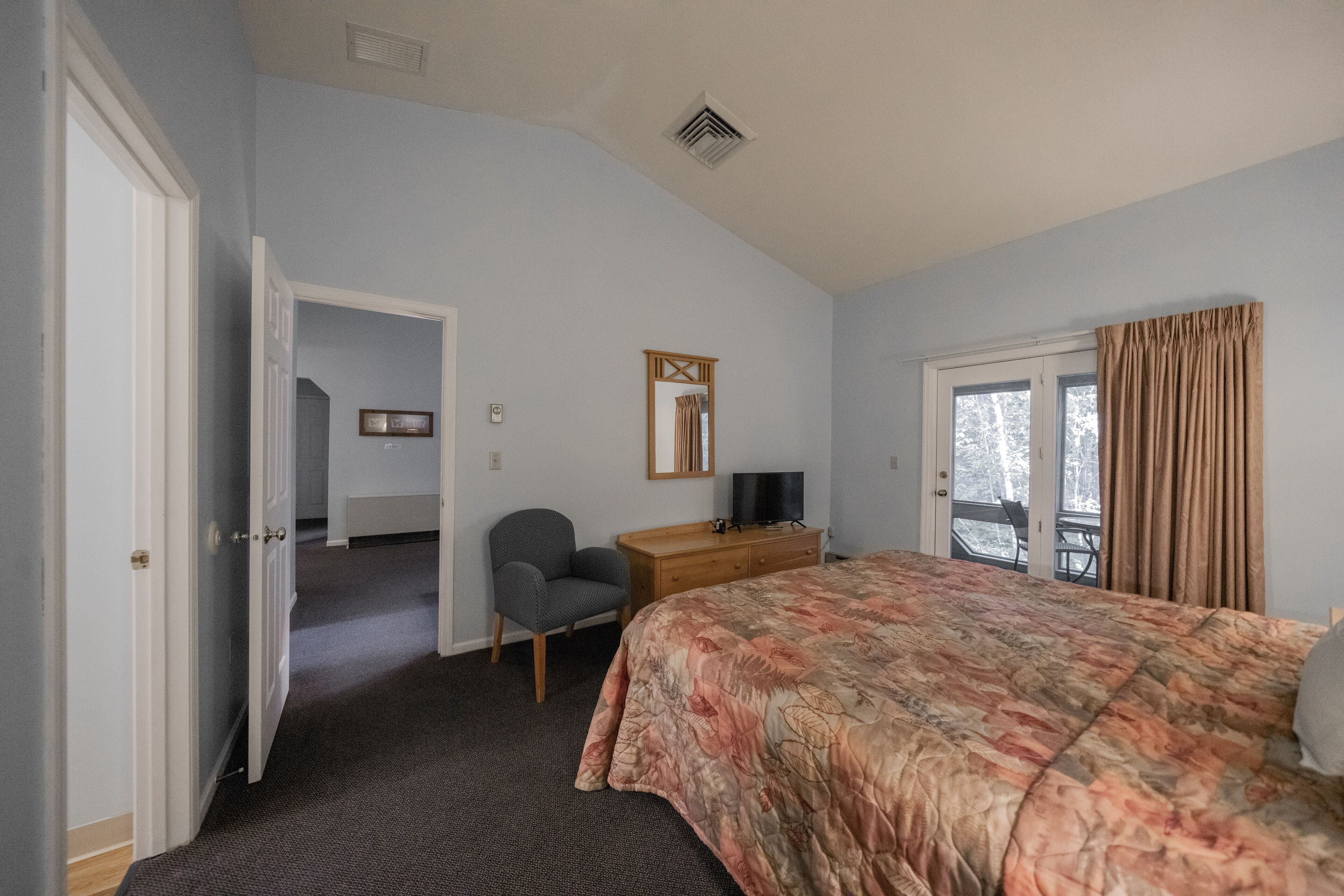 A bedroom with a bed, a desk, a chair, and a window with curtains.
