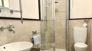 Un baño con un lavamanos grande de color blanco, una cabina de ducha de vidrio y un inodoro.