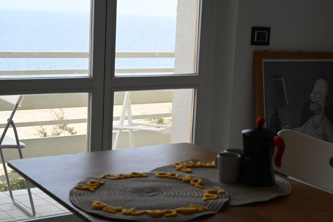 Una habitación con vistas al mar a través de amplios ventanales, una mesa con camino de mesa, una taza y una cafetera.