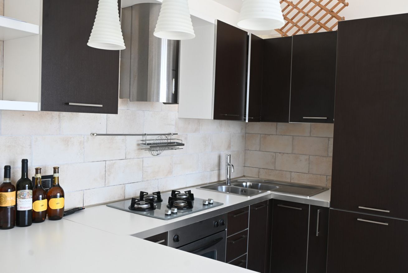Una cucina moderna con mobili scuri, un lavello in acciaio inox e un piano cottura a gas.