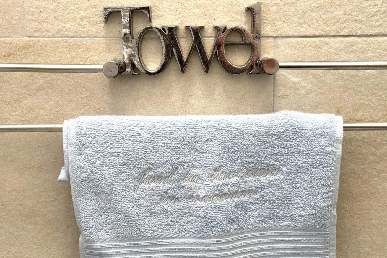 Un asciugamano appeso a un portascopevoli metallico, con la scritta 'Towel' sopra.