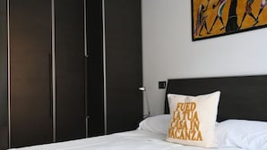 Un dormitorio con una cama, un almohadón con texto, un cuadro y un armario.