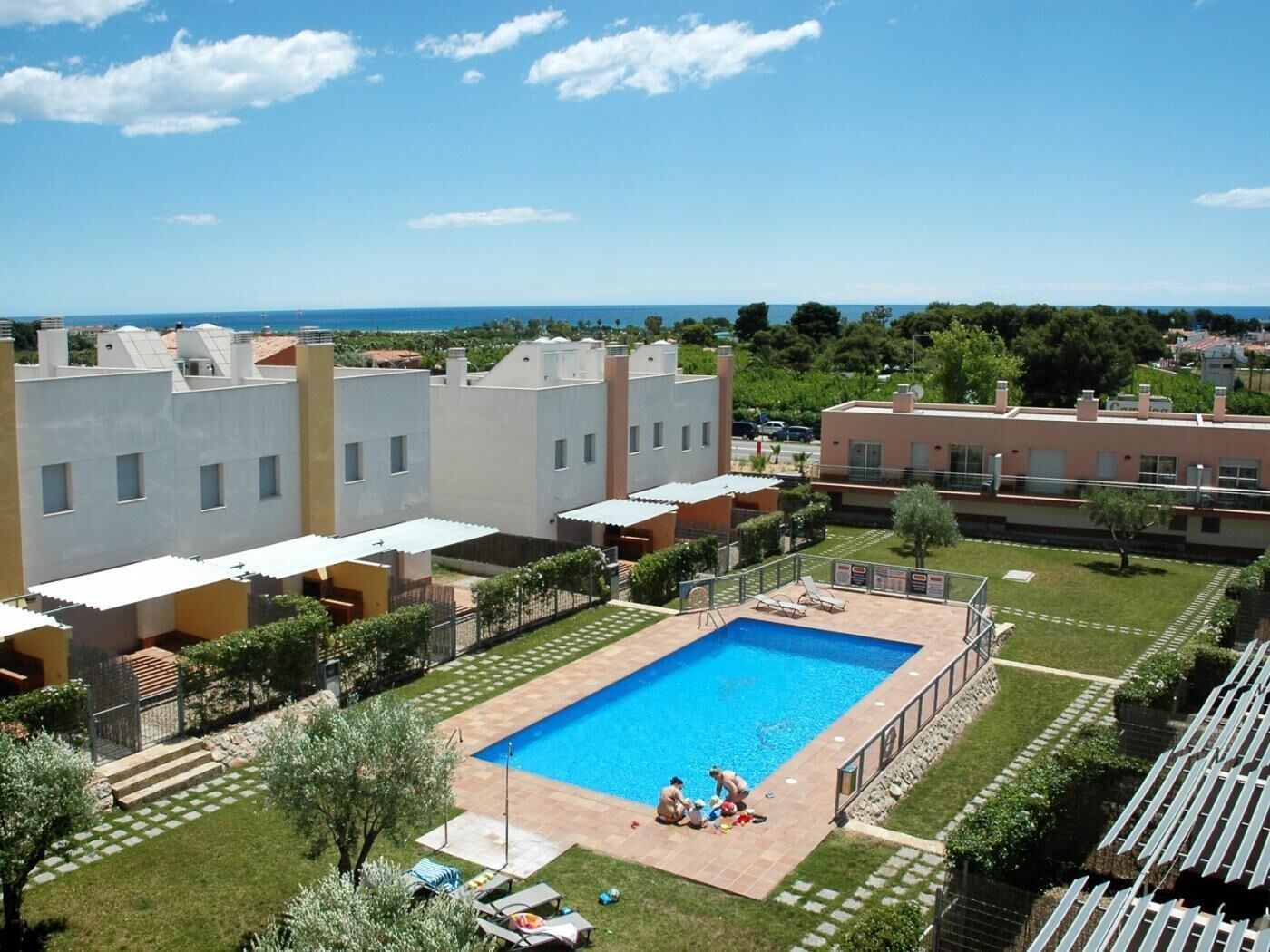 A residential area with a swimming pool surrounded by a well-maintained lawn and a view of the sea.