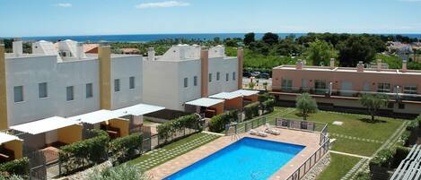 A residential area with a swimming pool surrounded by a well-maintained lawn and a view of the sea.