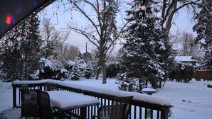 A snow-covered deck with outdoor furniture, surrounded by snow-laden trees and a house in the background. - Broadmoor Area Home Great for Families and Pets! (Colorado Springs)