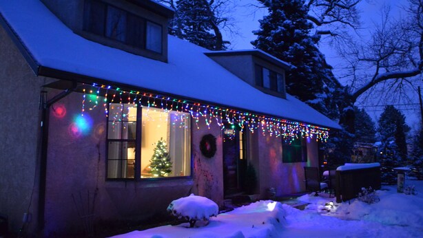 A house with snow on the roof and ground, a Christmas tree inside, and colorful lights on the exterior. - Broadmoor Area Home Great for Families and Pets! (Colorado Springs)
