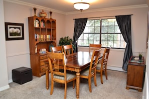 A dining room with a wooden table and chairs, a bookshelf, a framed picture, and a window with curtains. - Broadmoor Area Home Great for Families and Pets! (Colorado Springs)