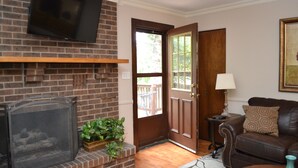 A living room with a brick fireplace, a television mounted above it, a brown leather sofa, and a door leading outside. - Broadmoor Area Home Great for Families and Pets! (Colorado Springs)