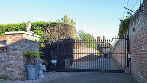Ein verschlossener Eingangsbereich mit einer Ziegelmauer, einem Metalltor und einer Hecke.