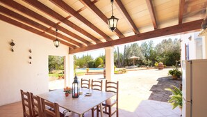 A covered patio with a wooden table and chairs, a lantern, and a view of a pool and garden. - Es figueral den Vicenç (Campos)