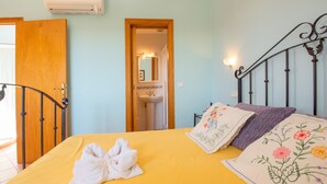 A bedroom with a yellow bedspread, a white towel, and floral pillows. - Es figueral den Vicenç (Campos)