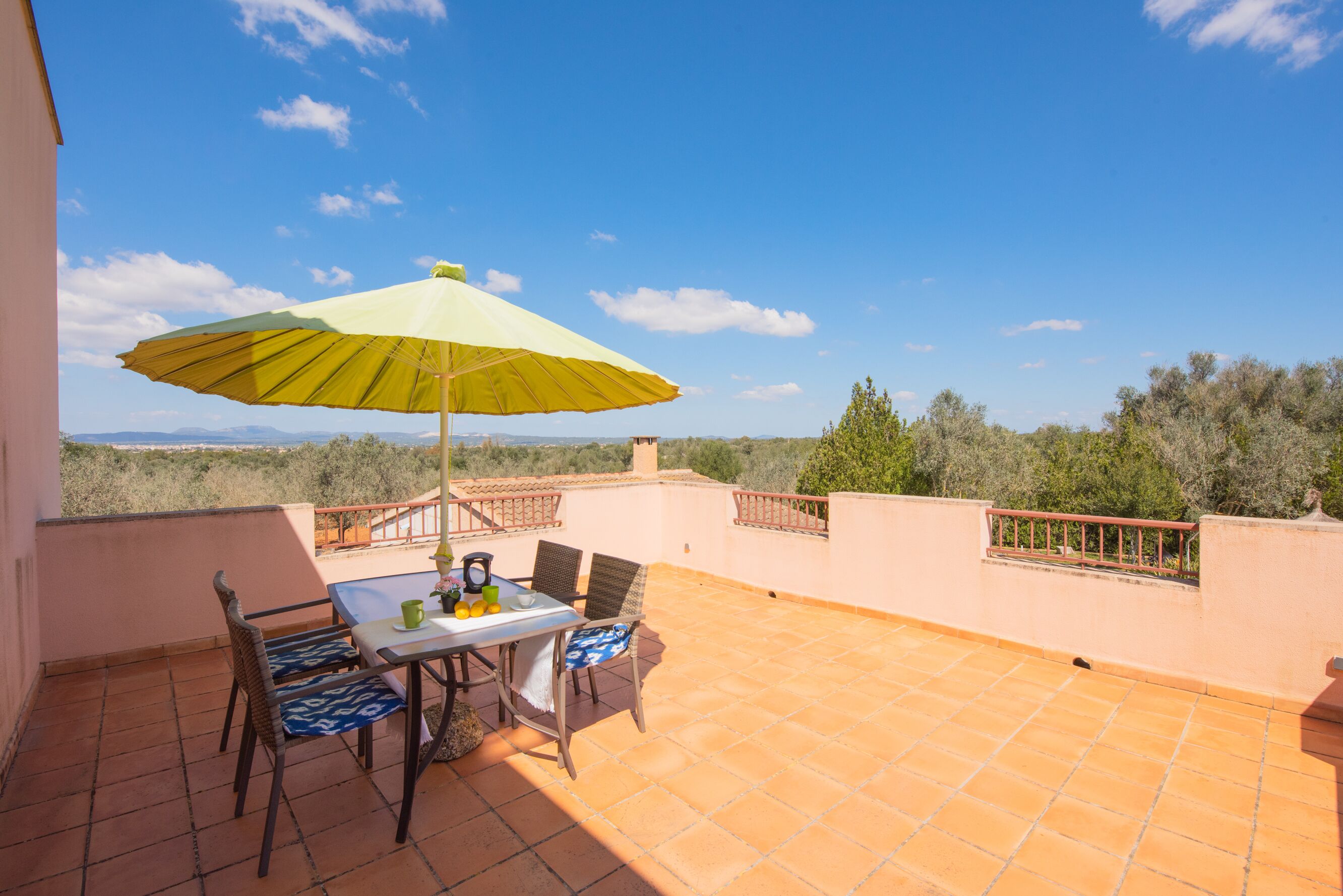 A terrace with a table and chairs, a yellow umbrella, and a view of the countryside.