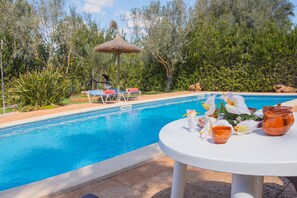 A poolside area with lounge chairs, a table with a drink and flowers, and a thatched umbrella. - Es figueral den Vicenç (Campos)