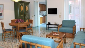 A living room with a dining table, chairs, a sofa, and a television. - Talè Talè Apartment just 90m from the sandy beach (Marina di Ragusa)