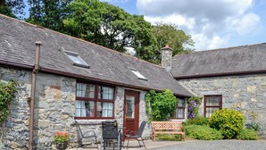 A stone cottage with a gravel driveway, a wooden bench, and a small garden with flowers and shrubs. - Low Cordorcan - UK5891 (Wood of Cree, near Newton Stewart)