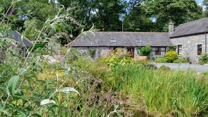 A stone cottage with a thatched roof, surrounded by lush greenery and a small pond. - Low Cordorcan - UK5891 (Wood of Cree, near Newton Stewart)