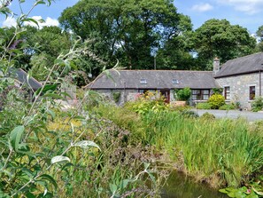 A stone cottage with a thatched roof, surrounded by lush greenery and a small pond. - Low Cordorcan - UK5891 (Wood of Cree, near Newton Stewart)