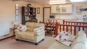 A living room with a beige armchair and sofa, a wooden cabinet, and a dining area with a table and chairs. - Low Cordorcan - UK5891 (Wood of Cree, near Newton Stewart)