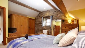 Une chambre à coucher avec un lit, une armoire en bois, une télévision et un mur en pierre.