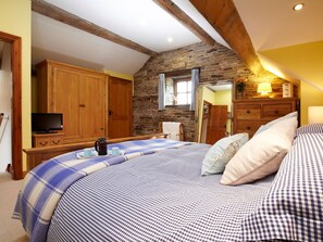 A bedroom with a bed, wooden wardrobe, television, and stone wall. - Birch Cottage - UK4185 (Millhouse Green, near Penistone)