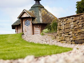 A wooden cottage with a thatched roof, a wooden door, and a stone wall.