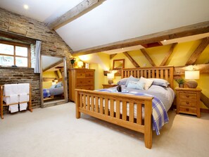 A bedroom with a wooden bed, a nightstand, a dresser, a mirror, and a stone wall.