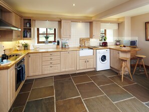 A kitchen with wooden cabinets, a washing machine, a microwave, and a sink. - Birch Cottage - UK4185 (Millhouse Green, near Penistone)