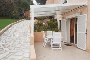 Un espace patio agrémenté d’un chemin en pierre, de mobilier d’extérieur blanc et d’un coin salon abrité.