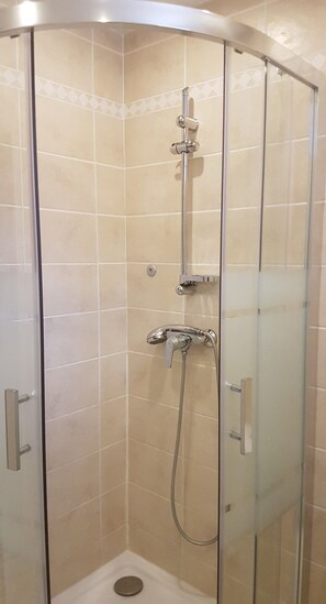 Une cabine de douche fermée par des parois en verre, dotée d’un pommeau de douche à main et d’un robinet fixé au mur.