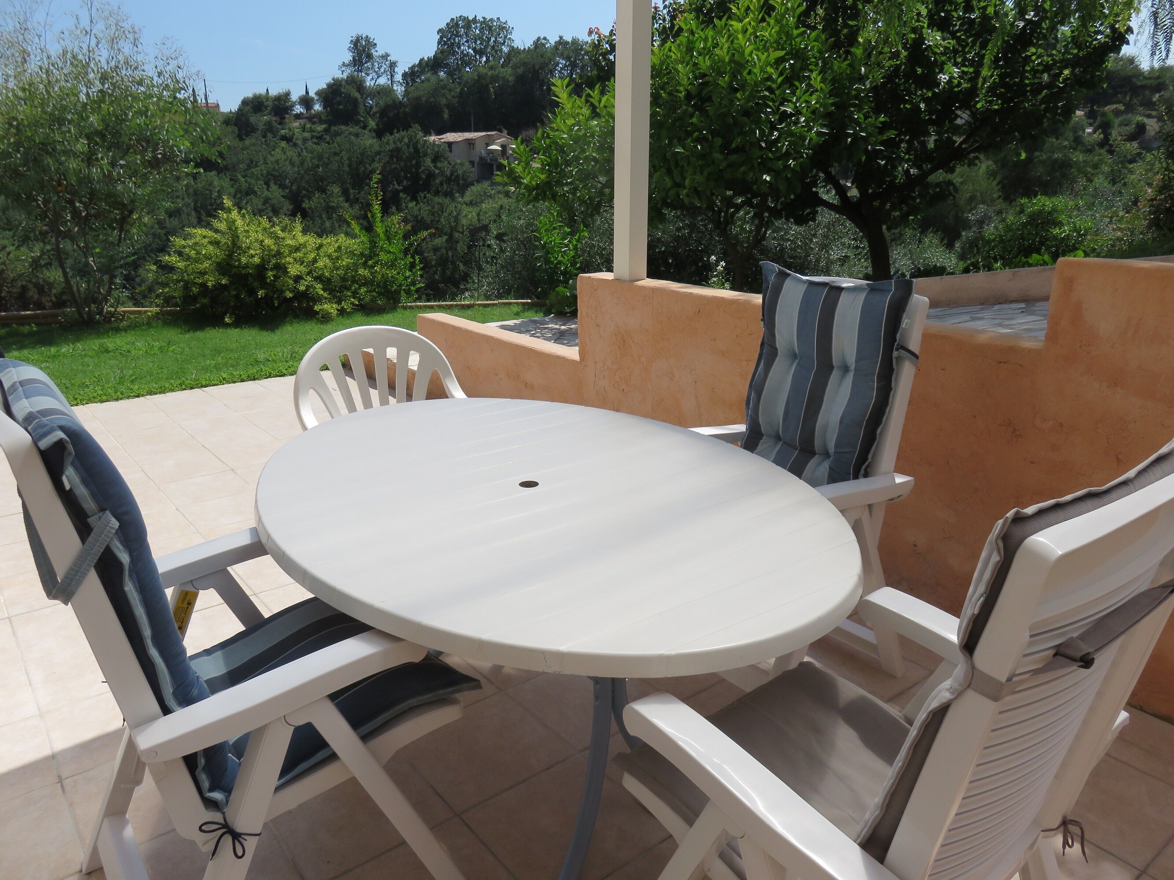 Ein Außenbereich mit einer Terrasse, einem runden Tisch und weißen Stühlen.