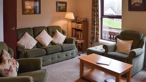 A cozy living room with a green sofa, a wooden coffee table, and a bookshelf. - 4 bedroom accommodation in Ambleside (Ambleside)