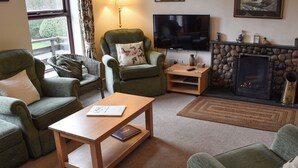 A cozy living room with green upholstered armchairs, a wooden coffee table, a flat-screen TV, a fireplace, and a stone wall. - 4 bedroom accommodation in Ambleside (Ambleside)