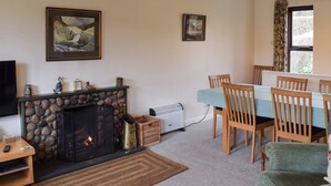 A living room with a stone fireplace, a dining table with chairs, a television, and framed artwork on the wall. - 4 bedroom accommodation in Ambleside (Ambleside)