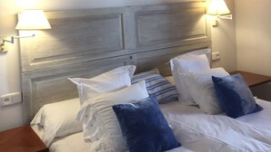 Habitación de hotel con cabecera de madera, dos lámparas de noche y cama con ropa de cama blanca y almohadas azules.