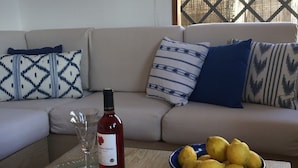 Una sala de estar con un sofá, cojines estampados, una botella de vino, una copa y un cuenco de limones sobre una mesa.