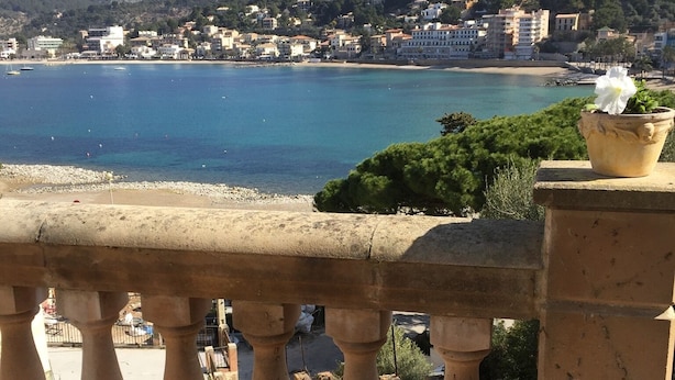 Un balcón con vistas a un pueblo costero, un regador de metal y una planta en maceta.