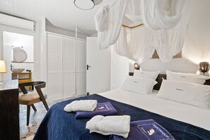 A hotel room with a bed, a desk, a chair, a wardrobe, and a bathroom visible through an open door.