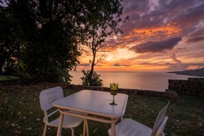 An outdoor seating area with a table and chairs, overlooking a sunset over the sea.