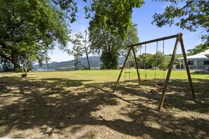 A swing set in a grassy area with trees and a view of mountains in the distance.