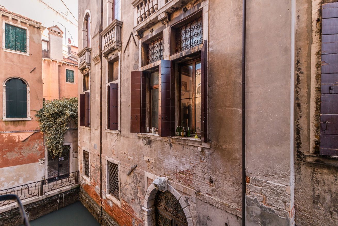 A narrow alleyway with old buildings, one with a visible window and a metal gate.