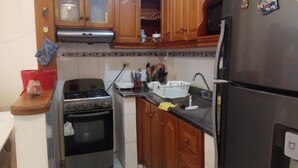 A compact kitchen with wooden cabinets, a gas stove, an oven, a sink, and a refrigerator. - Cozy and quiet room in family house (Cartagena)